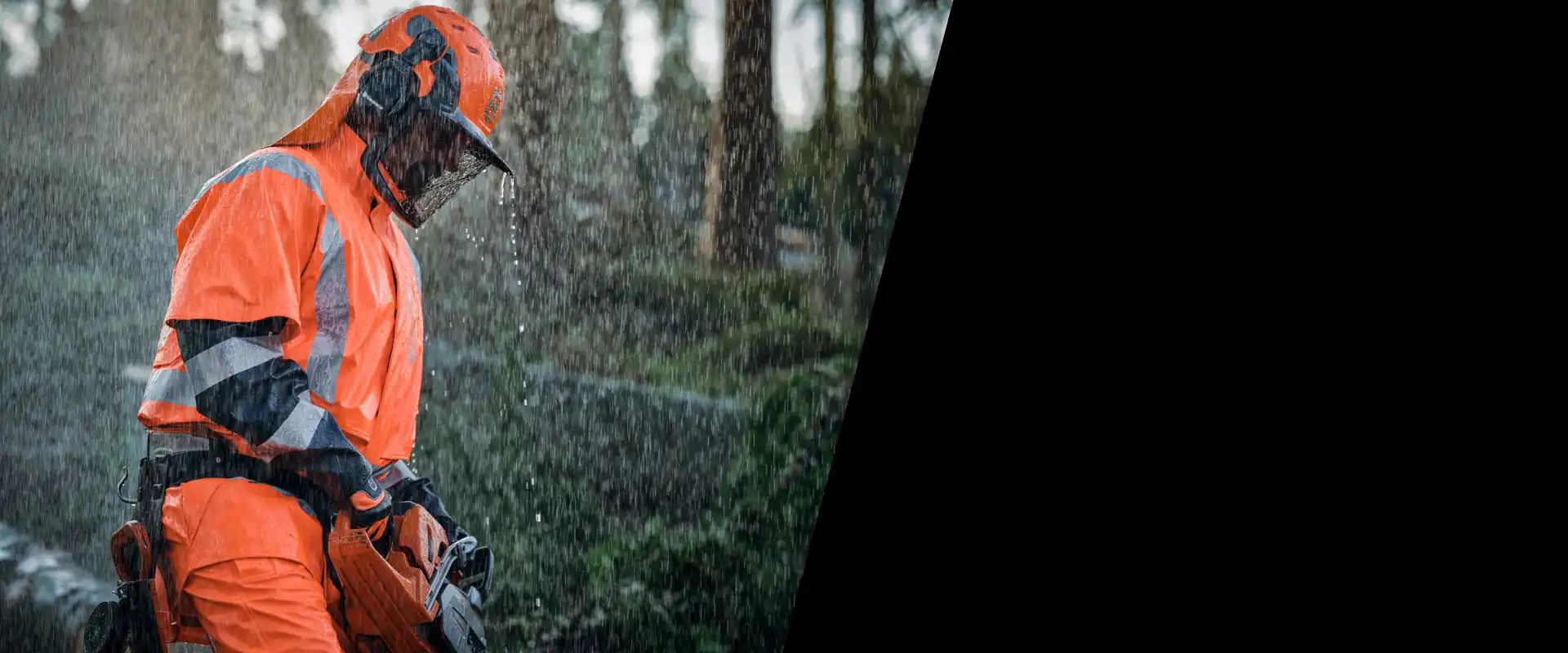 Forestry worker in orange protective gear operating a chainsaw in the rain.